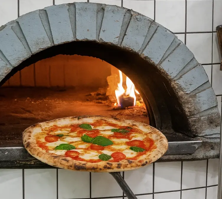 Pizza wird aus einem Steinofen herausgeholt